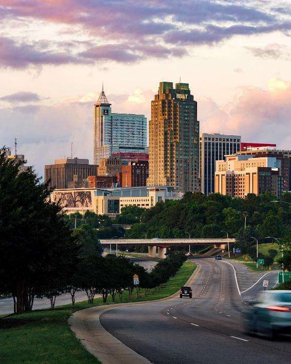 Coches conduciendo por la calle hacia edificios altos en el centro de Raleigh. Foto de @visitraleigh de usuario de Instagram