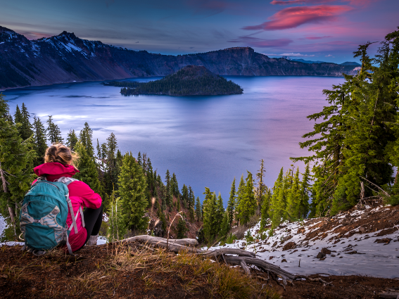 Una chica mochilera viendo el tranquilo Crater Lake en Oregon, una pieza sobre los mejores lagos de los Estados Unidos, al atardecer